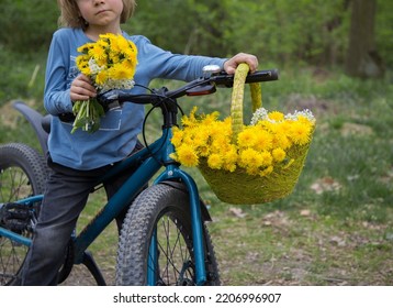 Unrecognizable Boy With A Blue Bicycle. On The Handle Hangs A Wicker Basket Full Of Spring Flowers - Yellow Dandelions. Mother's Day Gift For Mom. Stand With Ukraine. Active Interesting Childhood