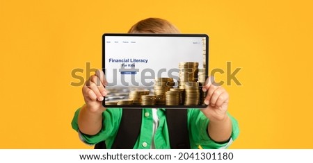 Unrecognizable boy holding tablet pc with Financial Literacy For Kids website in front of his face on orange studio background, banner design. Online economic education for children, money management
