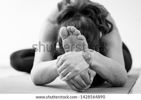 Unrecognizable brunette European woman on the floor practicing the Janu Sirsasana or Head-to-Knee Forward Bend, also known as a seated yoga pose. Black and white horizontal floor-level view.