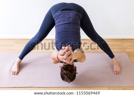 
An unrecognizable brunette woman in her 30’s practicing yoga at home. One woman concentrated on a aide-legged forward bend asana, or yoga posture. Horizontal view.  