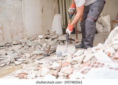 Unrecognizable builder collecting construction debris with a shovel. House renovation.