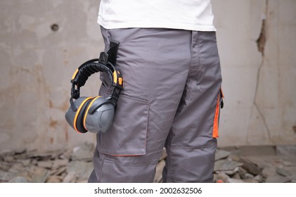 Unrecognizable Builder With Hearing Protection Hanging From The Trousers. Safety At Work Concept.