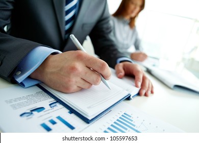 Unrecognizable Business Person Analyzing Graphs And Taking Notes