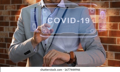 Unrecognizable businessman activates conceptual HUD holograms on smartwatch with text COVID-19. Man in jacket with holographic technology on wristwatch on background of brick wall