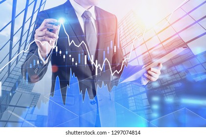 Unrecognizable businessman with clipboard drawing forex graph with glowing pen over skyscrapers background. Stock market concept. Toned image double exposure