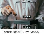 Unrecognizable businessman pulling small metal ball of Newton cradle and observing momentum over glass tabletop