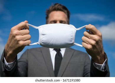 Unrecognizable businessman standing outdoors breathing fresh air holding a white surgical face mask under sunny blue sky - Powered by Shutterstock