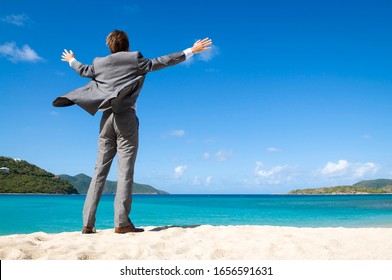 Unrecognizable businessman standing outdoors on tropical beach spreading his arms out into the wind