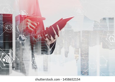 Unrecognizable businessman using tablet computer over cityscape background with double exposure of internet icons. Concept of hi tech in business. Toned image