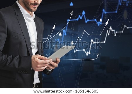 Unrecognizable businessman using tablet computer in blurry office with double exposure of financial graphs. Toned image