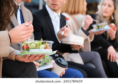 Unrecognizable businesspeople on lunch break talking while eating salad outside office building together. - Powered by Shutterstock