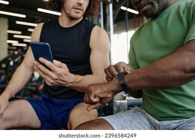 Unrecognizable caucasian athlete and unknown black man sitting at gym checking their gadgets - Powered by Shutterstock