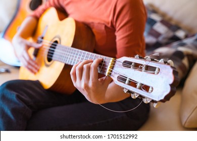 Unrecognizable Caucasian Female Learning How To Play An Instrument. Leisure And Music At Home Concept. Isolated Woman Playing The Guitar On The Couch Staying In The House. Music Lessons Indoors.