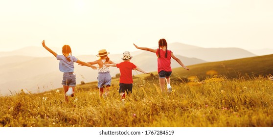 Unerkennbar fröhliche kleine Mädchen in ungezwungener Kleidung, die Spaß haben und bei Sonnenuntergang auf grünem Feld zusammen laufen, während sie Sommerferien auf dem Lande genießen