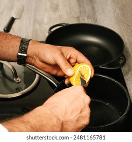 Unrecognizable chef squeezing a lemon over a saucepan in a modern kitchen
