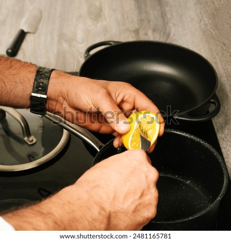 Unrecognizable chef squeezing a lemon over a saucepan in a modern kitchen