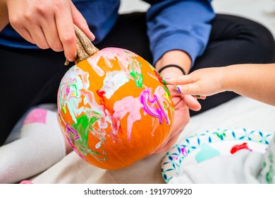 An Unrecognizable Child Finger Painting A Pumpkin With Colorful Paints While An Adult Holds It.