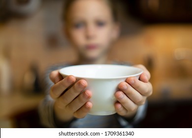 Unrecognizable child girl reaching out hands holding white empty bowl plate offering food or asking for food. Shallow focus. Giving concept. Hungry children