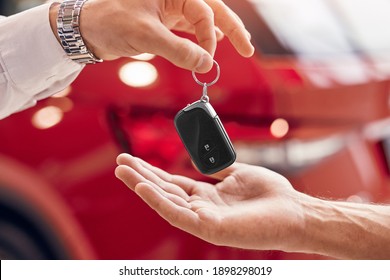 Unrecognizable client receiving keys of rent vehicle from manager against red vehicle in dealership - Shutterstock ID 1898298019