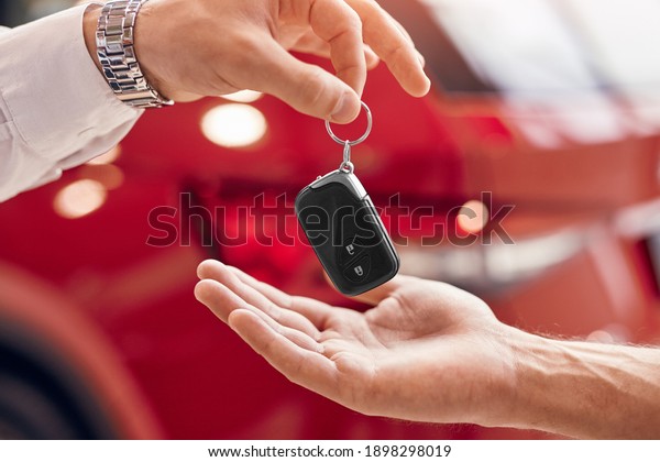 Unrecognizable client receiving\
keys of rent vehicle from manager against red vehicle in\
dealership