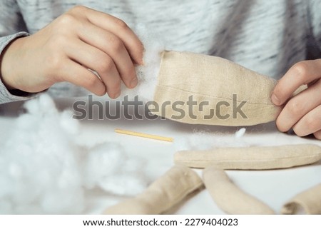 Unrecognizable closeup of woman designer hands sewing soft toys. Create paws and body part, stuffed them with cotton on table. Kid present shop, store. Small business, creative occupation and tutorial