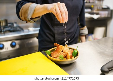 Unrecognizable cook sprinkling salt over a bowl of pork and hot peppers while working in the kitchen of a modern restaurant. Famous torreznos of Spanish cuisine