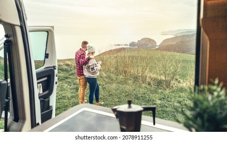 Unrecognizable couple traveling in camper van looking coastline landscape in the morning. Selective focus on couple in background