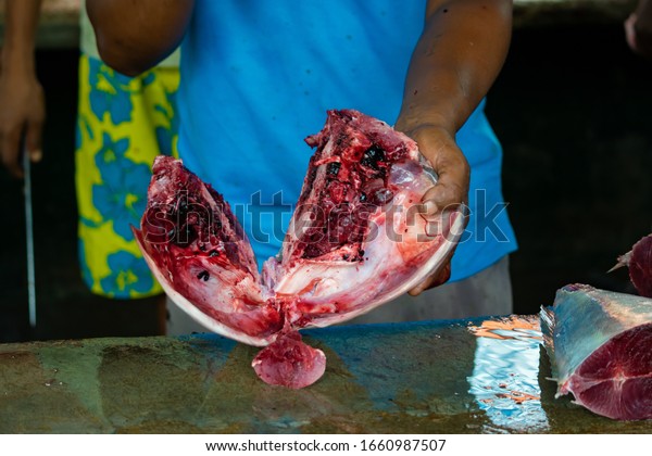 Unrecognizable creole man filleting and gutting\
fresh tuna fish at the street\
market.