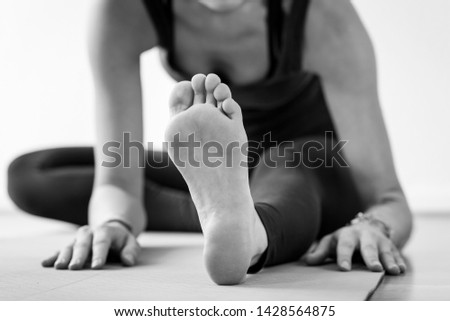 Unrecognizable cropped European woman on the floor on her way to Janu Sirsasana or Head-to-Knee Forward Bend, aka seated yoga pose. Black and white horizontal floor-level view of soles of yoga feet