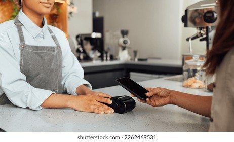 Unrecognizable customer paying by NFC at a cafe. Barista holding pos terminal while receiving payment. - Powered by Shutterstock