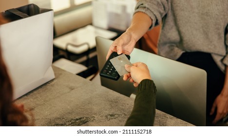 Unrecognizable Customer Paying With A Credit Card At The Checkout Counter. Woman's Hand Tapping A Bank Card On A Contactless Credit Card Reader. Woman Purchasing Clothes In A Clothing Store.