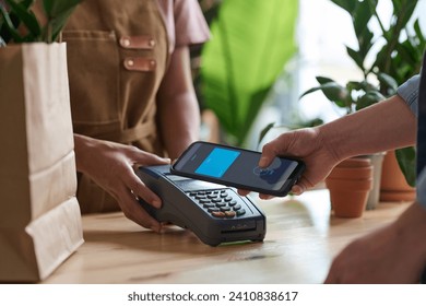 Unrecognizable customer using contactless way of payment with her smartphone at plant shot - Powered by Shutterstock