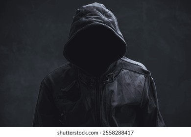 Unrecognizable cyber criminal or computer hacker wearing black hooded jacket, low key portrait, selective focus