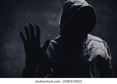 Unrecognizable cyber criminal or computer hacker wearing black hooded jacket, low key portrait, selective focus