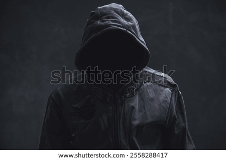 Unrecognizable cyber criminal or computer hacker wearing black hooded jacket, low key portrait, selective focus