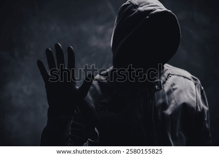 Unrecognizable cyber criminal or computer hacker wearing black hooded jacket, low key portrait, selective focus