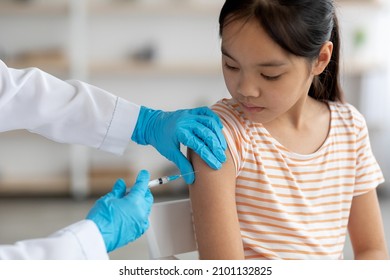 Unrecognizable doctor hands in protective gloves making vaccination against coronavirus of flu for little asian girl, home interior, closeup shot. Kids immunization against various disease concept - Powered by Shutterstock