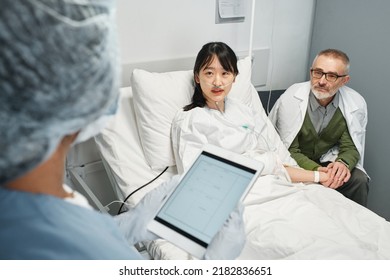 Unrecognizable doctor holding digital tablet talking to young Asian patient and her father in emergency room - Powered by Shutterstock