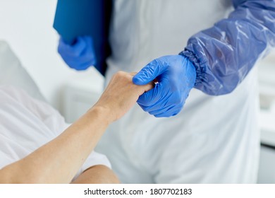 Unrecognizable doctor wearing protective gloves holding hand of senior woman in hospital ward
