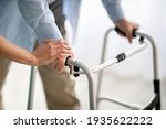 Unrecognizable elderly man using walker, young doctor supporting and helping him at retirement home