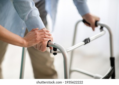 Unrecognizable elderly man using walker, young doctor supporting and helping him at retirement home