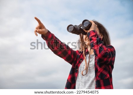 Unrecognizable explorer young woman looking trough binoculars and pointing with her finger