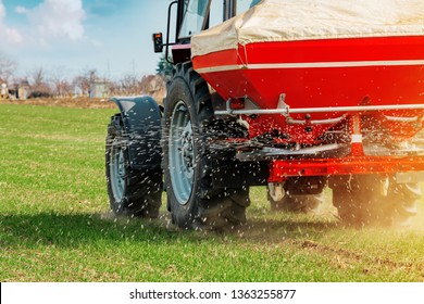 Unrecognizable Farmer In Agricultural Tractor Is Fertilizing Wheat Crop Field With NPK Fertilizer Nutrients