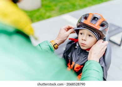 Unrecognizable Father Help Son Dressing Cap, Cute Caucasian Boy Kindergarten Student Wearing Helmet In A Bicycle Seat With His Father. Kid Waiting For The Riding. Child Safety And Protection Concept.