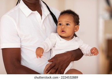 Unrecognizable Father Holding Little Cute Black Infant Boy In Hands, Portrait Of Adorable African American Baby Looking Away With Curious Face Expression, Bonding With Dad At Home, Closeup