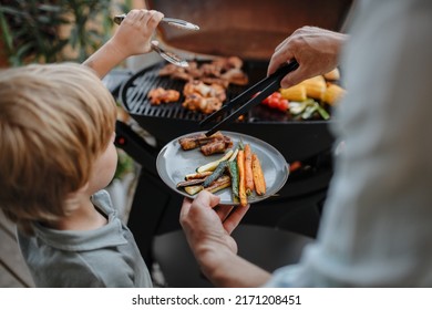 Unrecognizable father with little son grilling ribs and vegetable on grill during family summer garden party, close-up - Powered by Shutterstock