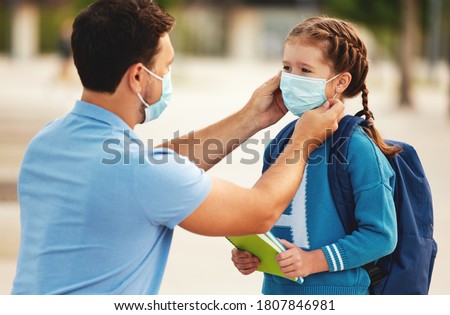 Unrecognizable father putting medical mask on face of cheerful schoolgirl while preparing for school during coronavirus pandemic
