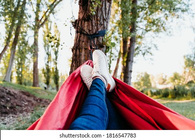 Unrecognizable Feet Of Woman Relaxing In Orange Hammock. Camping Outdoors. Autumn Season At Sunset. POV