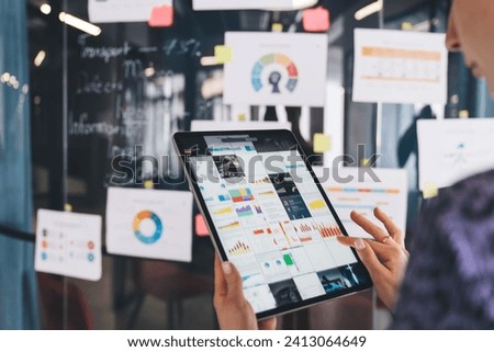 Unrecognizable female analyst browsing business infographics during working process with statistics online report on digital tablet, trader checking web graphic charts via app on modern touch pad