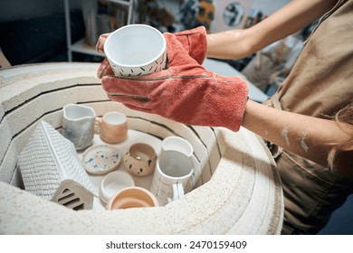 Unrecognizable female artisan taking glazed mug from kiln - Powered by Shutterstock